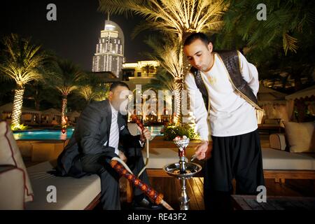 Mann Rauchen einer Wasserpfeife, Shisha, am Pool am Abend, das Palace Hotel, Altstadt, Dubai, Vereinigte Arabische Emirate, Naher Osten Stockfoto