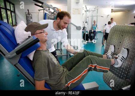 Patienten, die in den Muskeln Training auf verschiedenen Maschinen in einer Turnhalle, Physiotherapie, Physikalische Therapie in einer neurologischen Stockfoto