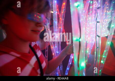 Jungen in einem Irrgarten, Labyrinth aus bunt beleuchteter Stangen, auf einer Messe Stockfoto