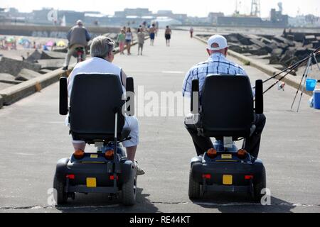 Senioren auf motorisierte Rollstühle auf einer konkreten Wellenbrecher am Strand von Scheveningen, Strand Stadtteil von Den Haag, Stockfoto