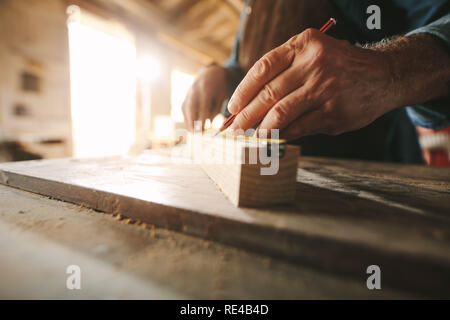 In der Nähe der Hände des Älteren Tischler dabei einige Markierungen auf Bar aus Holz mit Maßband und Bleistift. Stockfoto