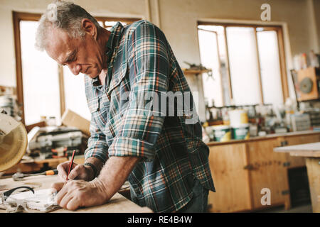 Qualifizierte kaukasischen männliche Tischler, Zeichnungen auf der Zwischenablage. Eigentümer des Handwerks Workshop die wenigen Möbel Skizzen. Stockfoto