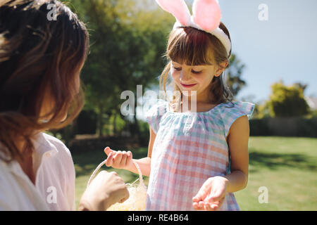 Kleines Mädchen tragen Kaninchen ohr-kopfband in einem Garten mit einem Korb stehen. Mutter und Tochter spielen im Garten an einem sonnigen Tag. Stockfoto