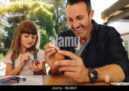 Lächelnd mann Malerei Ostereier. Kleines Mädchen Malerei Ostereier mithilfe eines Pinsels sitzt mit ihrem Vater. Stockfoto