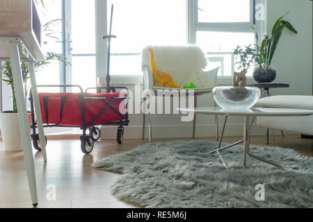 Rot faltbarer Wagen in helles Apartment Wohnzimmer, mit Dinosaurier Spielzeug sitzt auf einem Stuhl. Grau Fellimitat Teppich auf dem Boden. Stockfoto