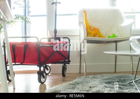 Rot faltbarer Wagen in helles Apartment Wohnzimmer, mit Dinosaurier Spielzeug sitzt auf einem Stuhl. Grau Fellimitat Teppich auf dem Boden. Stockfoto