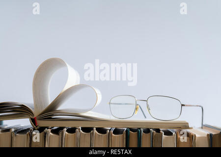 Alte hard cover Buch Seite schmücken Herzform mit Brille auf der Seite für die Liebe am Valentinstag mit unscharfen Hintergrund und kopieren Sie Platz für Text. C Stockfoto