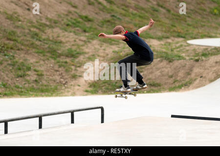 Junge skateboard Sportler tut ein Sprung in eine konkrete Skatepark. Extreme Sport Freizeitbeschäftigung für die Jugend. Mann tut einem Stunt auf einem Skateboard Stockfoto