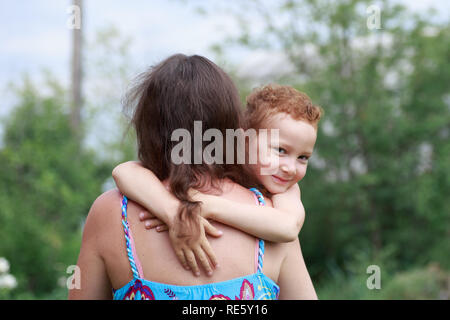 Portrait von lustigen rothaarige Junge mit den Sommersprossen Umarmungen seiner Mutter um den Hals. Stockfoto