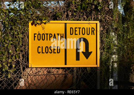 Wanderweg geschlossen und Umweg helle gelbe Sicherheit Straßenschild hängend an einem Zaun durch Wachstum. Stockfoto