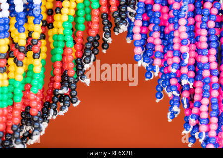 Detail der traditionellen wulstige Kostüm für den Verkauf in einem Markt in Südafrika. Strings mit bunten Perlen hängen gegen orange hinterlegt. Stockfoto