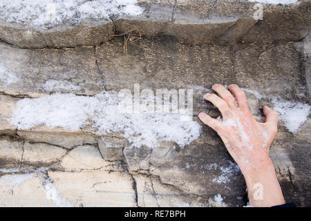 Die Hand eines Mannes klammert sich an einer Leiste auf einen Stein. Stockfoto