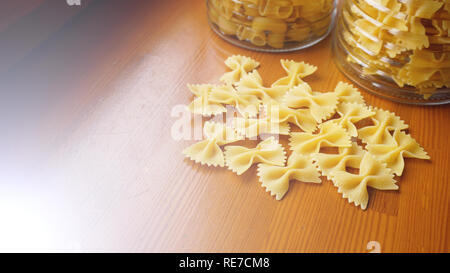 Nudeln in Form von Bögen aus Glas Glas verstreut. Italienische Pasta Stockfoto