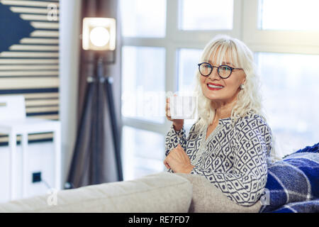 Schöne positive Frau nimmt einen Schluck Tee Stockfoto