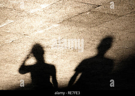 Unscharfe Reflexion Schatten von zwei Leuten auf Sommer glänzende sonnigen Bürgersteig in sepia schwarz und weiß Stockfoto