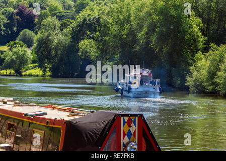 Kreuzfahrt entlang der Themse auf einem Motorboot mit einem schmalen Boot, das im Vordergrund im Dorf Goring-on-Thames, South Oxfordshire, England, festgemacht ist Stockfoto
