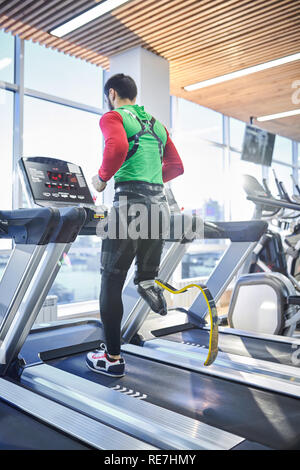 Ansicht der Rückseite des jungen behinderten Mann mit Fitness Beinprothese laufen auf Laufband, während allein die Ausbildung in modernen Fitnessraum Stockfoto