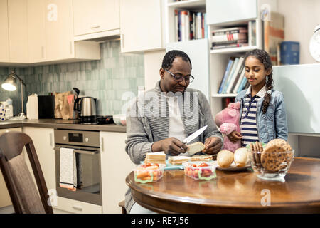 Süße Tochter mit rosa Spielzeug aufpassen Vater kochen Frühstück Stockfoto