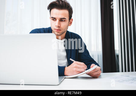 Konzentriert man schreiben neue Ideen in Notepad Suche auf dem Bildschirm Laptop. Junge Mitarbeiter sitzt am Tisch und die Arbeit im Büro Stockfoto