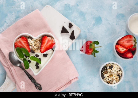 Joghurt mit Müsli und Erdbeeren in eine Herzförmige Schale auf einem hellen Hintergrund. Stockfoto