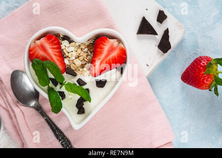 Joghurt mit Müsli und Erdbeeren in eine Herzförmige Schale auf einem hellen Hintergrund. Stockfoto