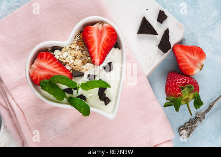 Joghurt mit Müsli und Erdbeeren in eine Herzförmige Schale auf einem hellen Hintergrund. Stockfoto