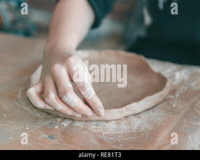 Weibliche Keramiker Hände machen trendige Platte von braun Ton. Nahaufnahme der Finger gemacht Mode Dessert flache Platte für das Handwerk Werkstatt. Stockfoto