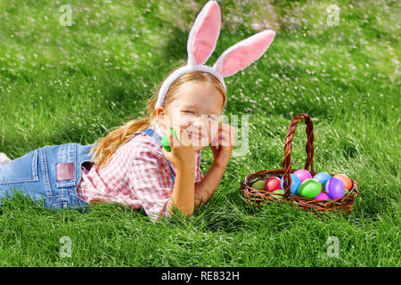 Glückliche kleine Mädchen am Tag der Ostern ist auf der Suche nach bunte Eier in einem Korb und Falten Stockfoto