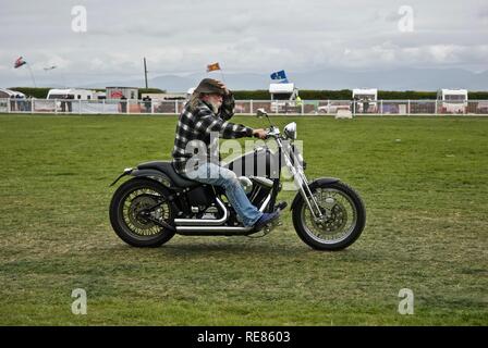 Mann mit einem weißen Bart hält auf seinen Hut, wie er reitet seine Harley Davidson Low Rider Fahrrad an der Oldtimer Rallye Mai 2010 Anglesey Anglesey, Wales, Großbritannien Stockfoto