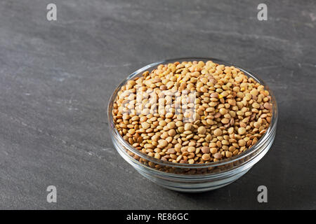 Roh Linsen in eine Glasschüssel auf Schwarz Stein Hintergrund. Gesunde vegetarische Essen Konzept. Superfoods. Kopieren Sie Platz. Linsen sind reich an komplexen carbohydra Stockfoto