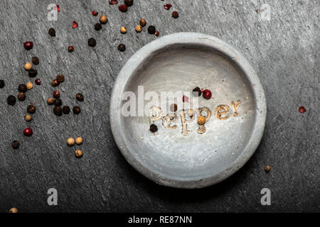 Schwarzer Pfeffer in kleine Schüssel für Gewürze auf dunklem Hintergrund. Roter, Grüner und schwarzer Pfeffer Körner close-up und Tageslicht. Dunklen Stein Hintergrund ein Stockfoto