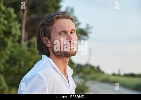 Portrait des jungen gutaussehenden brutalen Mann mit dem langen Haar, blaue Augen, eine einfache Borsten, er ist in ein weißes Hemd mit kurzen Ärmeln angezogen Stockfoto