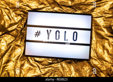 Text YOLO auf weiß beleuchtet. Sie leben nur einmal Konzept und Hashtag. Gelb glänzend Hintergrund. Stockfoto