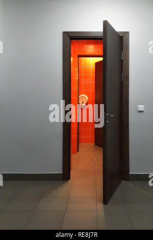 Die Tür zum Badezimmer mit orange Kacheln geöffnet auf dem Hintergrund der graue Wand. Stockfoto