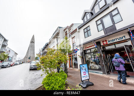 Reykjavik, Island - 19. Juni 2018: Leute, Touristen zu Fuß auf der Straße mit nassen Straße und Bürgersteig in der Innenstadt von Center und der berühmten Kirche Hallgrimskirkja Stockfoto