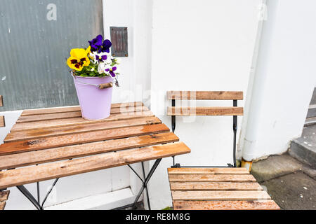 Leere Holz- Tisch draußen Restaurant Cafe mit Stühlen auf Bürgersteig und Straße Purpur Gelb Stiefmütterchen Blumen im Blumentopf Topfpflanze Einstellung mit nobod Stockfoto