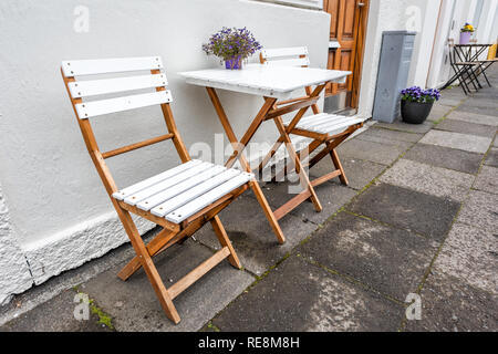 Weiße leere Holz- Tisch draußen Restaurant Cafe mit zwei Stühle auf dem Bürgersteig Straße und violetten Blüten in Blumentopf Topfpflanze Einstellung mit niemandem, ich Stockfoto