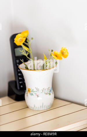 Nahaufnahme der altmodischen Keramik Porzellan Blumenvase mit gelben Pflanzen und Festnetztelefon auf hölzernen Tisch im Zimmer Ecke Stockfoto
