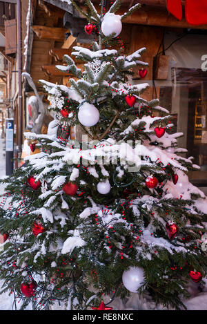 Ein großer Weihnachtsbaum mit roten Kugeln, Herz, Schnee und weisse kreisrunden Licht auf einer Straße in Morzine Haute Savoie Portes du Soleil Frankreich Stockfoto