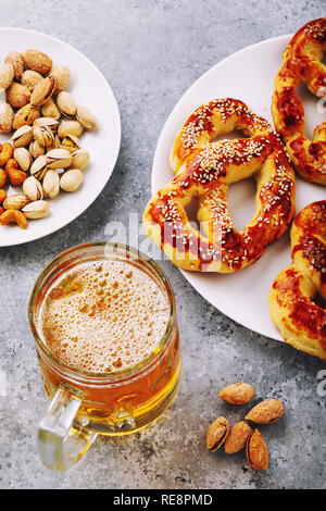 Glas frischen hellen Bier mit gesalzene Brezeln und Nüsse auf dem Tisch Stockfoto