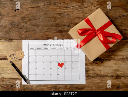 Konzeptionelle Bild von 2019 Februar Kalender und Gegenwart Geschenk mit roter Schleife auf rustikalen vintage Tabelle in sich bereit für Saint Valentines Tag gewickelt Stockfoto