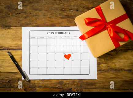 Konzeptionelle Bild von 2019 Februar Kalender ein Herz auf dem 14. und Gegenwart Geschenk verpackt mit roter Schleife auf rustikalen vintage Tisch bereit für Saint Valen Stockfoto