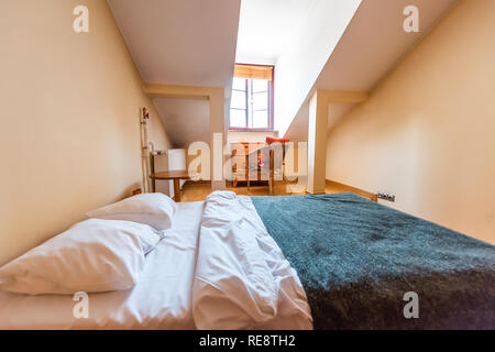 Neue, saubere europäische Doppelzimmer französisches Bett mit Dachschräge und Fenster im Loft mit Tisch und Kissen im Schlafzimmer Startseite Appartements Zimmer Stockfoto