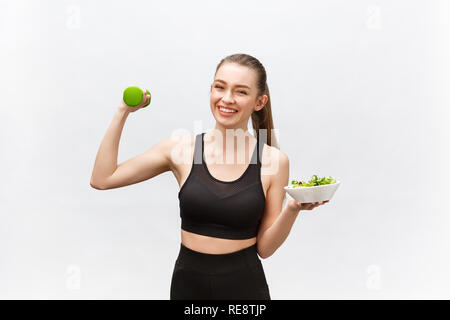 Sport, gesunder Lebensstil, Personen Konzept - Junge brünette Frau mit Salat und eine Hantel. Sie lächelt und geniessen die gesunde Lebensweise. Stockfoto