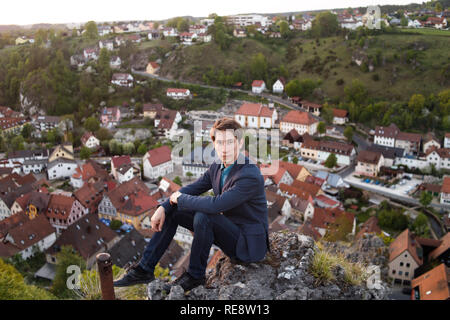 Ein Mann im Anzug sitzt auf dem Aussichtsdeck und betrachtet die Aussicht auf die Altstadt Häuser von oberhalb der historischen Altstadt von Pottenstein in Deutschland. Stockfoto