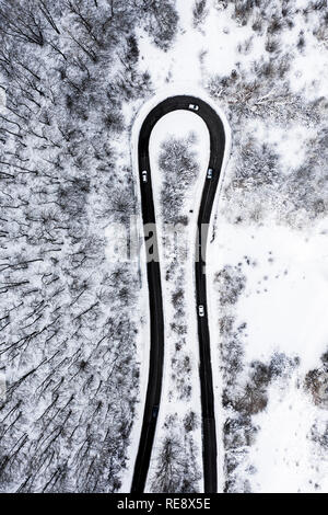 Luftaufnahme von einer schönen Serpentinenstraße mit einigen Autos, die durch Ausführen. Spektakuläre Landschaft, bestehend aus einem Pinien Wald und weißen Schnee. Stockfoto