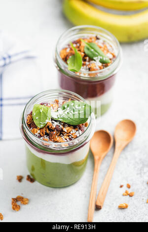 Grüne Smoothie in Glas mit Müsli und Spinat gekrönt. Gesundes Frühstück Parfait mit Avocado, Spinat, Joghurt und Berry Smoothie Stockfoto