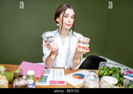 Junge Frau ernährungsberaterin nach Chia Pudding die Wahl zwischen gesunden Essen und süßes Dessert am Tisch voll von verschiedenen Produkten sitzen Stockfoto