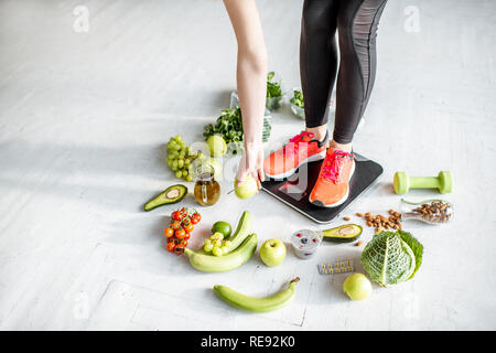 Sport Frau wiegen auf der Waage mit gesunden Lebensmitteln um. Gewichtsverlust, gesundes Essen und Sport Lifestyle Konzept Stockfoto