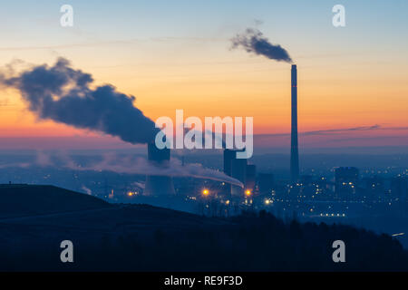 Dampf steigt aus einem Schornstein auf eine Fabrik gegen das Sonnenlicht bei Sonnenaufgang Silhouette Stockfoto